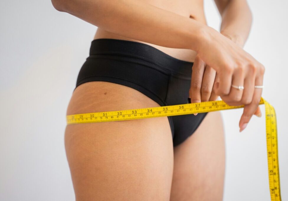 A person in black underwear measures their waist with a yellow tape measure.